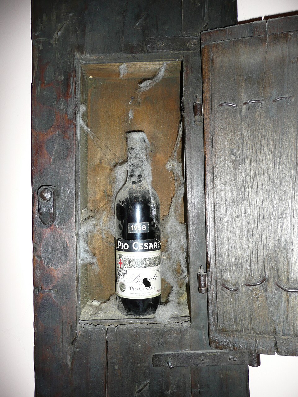 古い木の戸棚に置かれた、くもの巣をかぶったバローロの瓶。ラベルに1958の年が見える