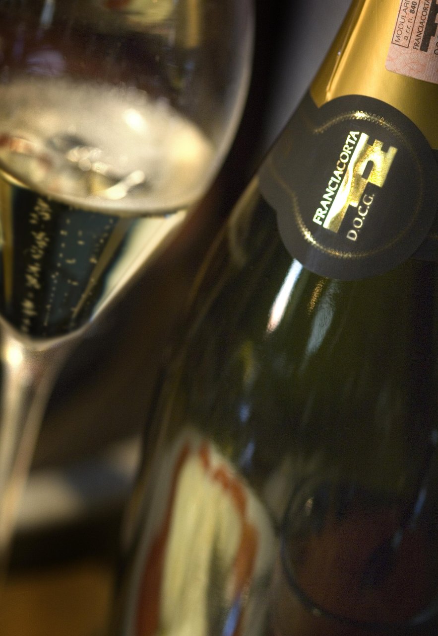 泡の立つグラスの横に、首に「FRANCIACORTA D.O.C.G.」と上が城壁の形のFの印がついた瓶